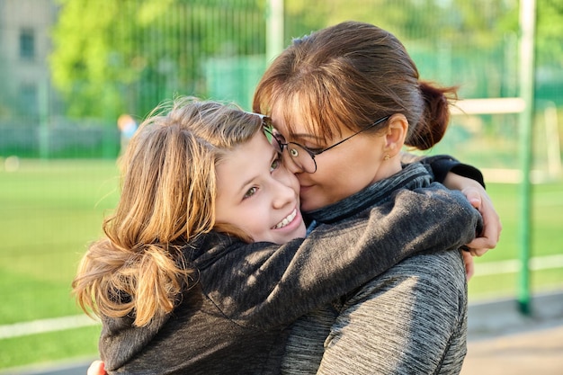 Portrait d'une maman heureuse et d'une fille préadolescente serrant ensemble en plein air