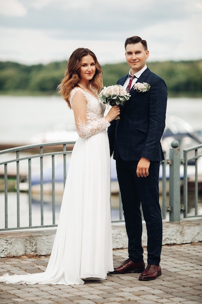 Portrait de marié en costume noir avec belle mariée en robe blanche dans le parc se dresse près du lac