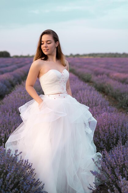 Portrait de la mariée dans un champ de fleurs de lavande vêtue d'une robe blanche. Fille dans les buissons de lavande en été. Bonne journée de mariage dans la nature.
