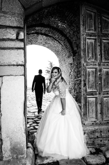 Photo portrait de la mariée avec le doigt sur les lèvres debout dans l'allée avec le marié marchant en arrière-plan