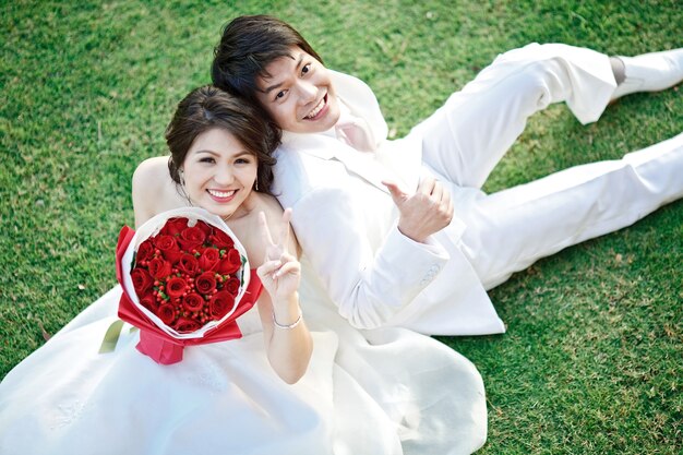 Portrait de la mariée et le marié assis sur l&#39;herbe fraîche avec bouquet de rose