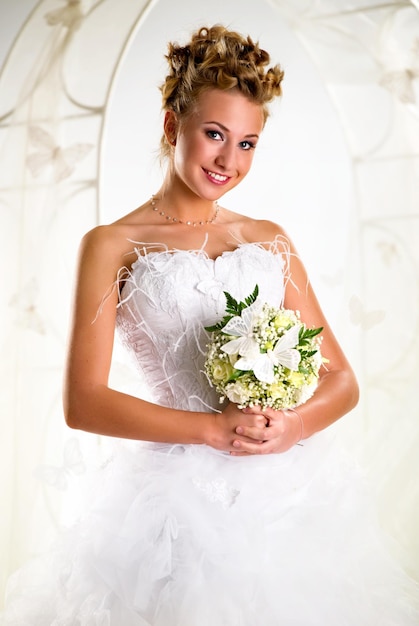 Portrait d'une mariée souriante tenant un bouquet tout en se tenant contre l'arc