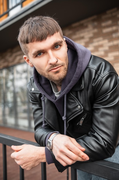 Le portrait masculin d'un beau mec hipster élégant avec des cheveux et une barbe portant des vêtements décontractés à la mode se dresse dans la rue