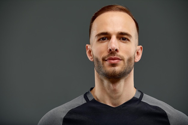 Portrait masculin en studio d'un beau modèle d'homme athlétique puissant avec un corps musclé sain dans un débardeur noir à la mode maquette pose sur un fond gris