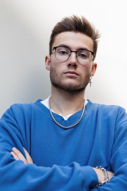 Portrait masculin urbain de beau jeune homme hipster avec des lunettes en sweat-shirt de mode bleu se dresse sur un fond blanc