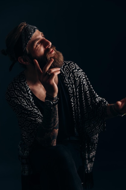 Portrait d'un mec avec une barbe et des tatouages sur un hipster de fond sombre