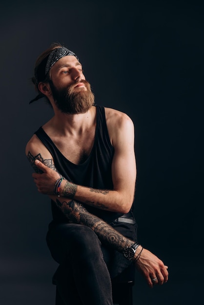 Portrait d'un mec avec une barbe et des tatouages sur un hipster de fond sombre