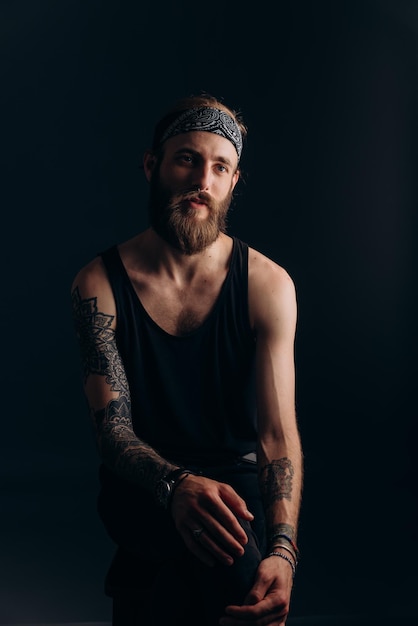 Photo portrait d'un mec avec une barbe et des tatouages sur un hipster de fond sombre