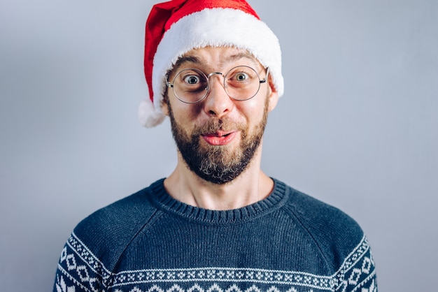 Portrait d'un mec barbu en bonnet de Noel et lunettes à la surprise