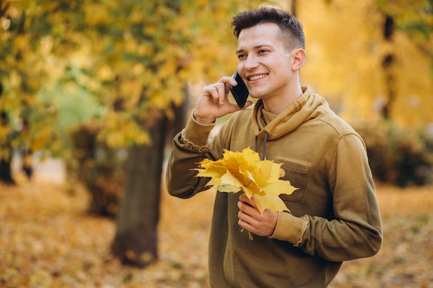 Portrait de mec beau et heureux souriant et parlant au téléphone dans le parc de l'automne