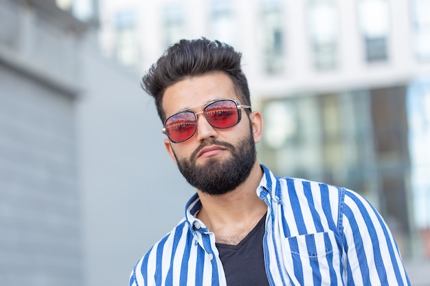 Portrait de mec étudiant élégant positif gai dans des verres avec une moustache et une barbe à l'extérieur.