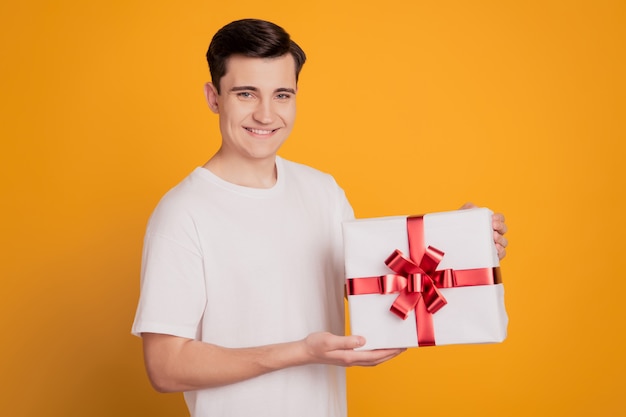 Portrait de mec mignon positif tenir une grande boîte-cadeau sourire rayonnant sur fond jaune