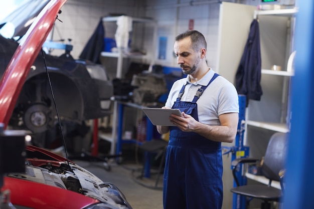 Portrait de mécanicien automobile barbu à l'aide de tablette numérique lors de l'inspection du véhicule dans un garage, espace copie