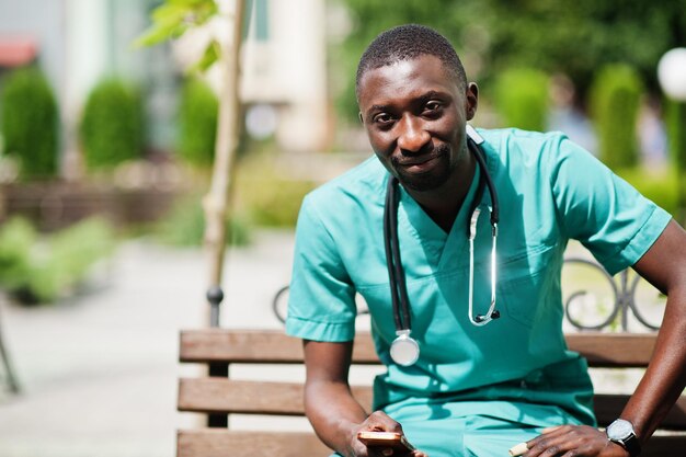 Portrait d'un médecin africain avec un stéthoscope portant un manteau vert avec un téléphone portable à portée de main.