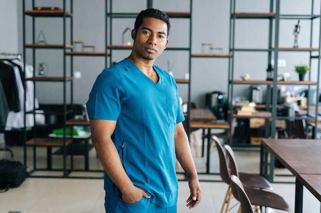 Portrait d'un médecin afro-américain confiant portant un uniforme de laboratoire médical de chirurgien bleu debout dans le bureau de l'hôpital regardant la caméra