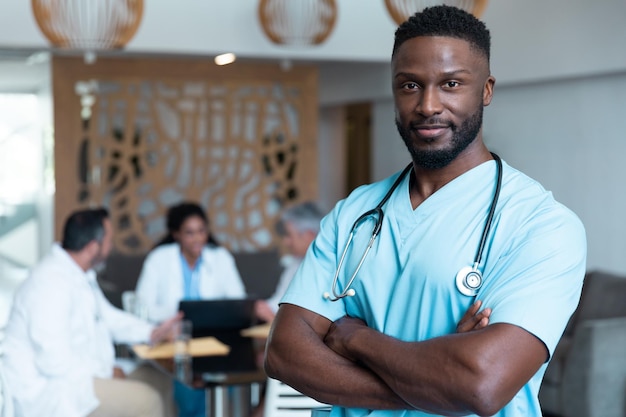Portrait d'un médecin afro-américain souriant, avec des collègues en discussion en arrière-plan