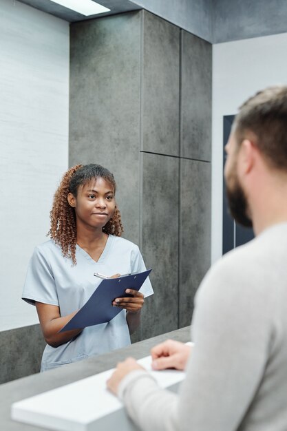 Portrait d'un médecin d'âge moyen souriant avec table et jeune infirmière debout dans la chambre des patients