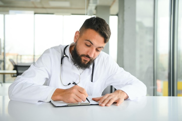 Portrait d'un médecin arabe beau jeune homme en vêtements de travail posant dans une clinique moderne assis au bureau