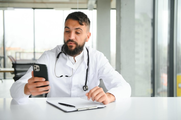 Portrait d'un médecin arabe beau jeune homme en vêtements de travail posant dans une clinique moderne assis au bureau