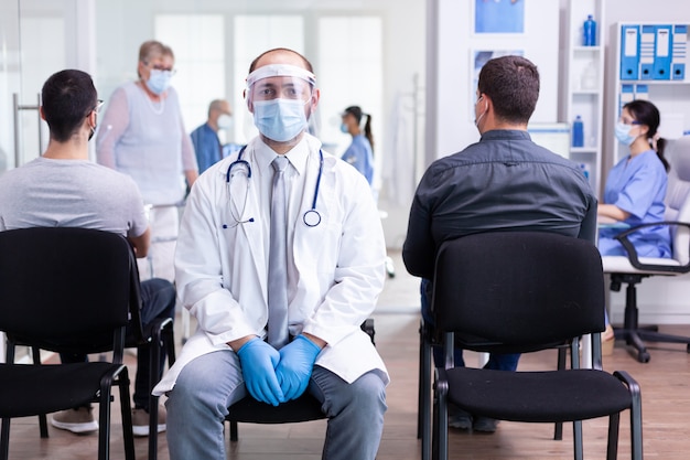 Portrait d'un médecin fatigué avec un masque facial et une visière regardant la caméra dans la zone d'attente de l'hôpital