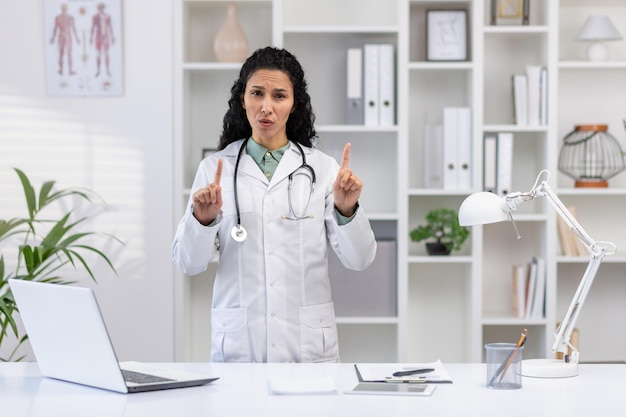 Portrait d'une médecin à l'intérieur d'un bureau de clinique. Une femme malheureuse et contrariée regardant la caméra qui pointe.