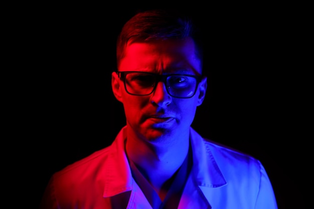 Portrait d'un médecin ou d'un médecin spécialiste. Portrait horizontal en taille réelle. Homme en gommage. Fond noir avec lumière bleue et rouge. Fermer.