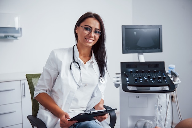 Portrait d'un médecin obstétricien assis dans la salle de la clinique avec un appareil à ultrasons.