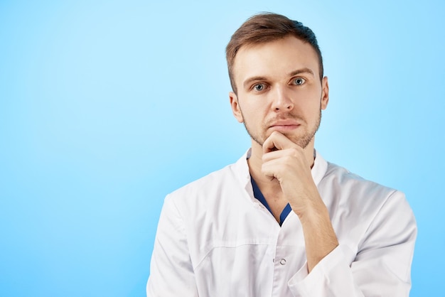 Portrait d'un médecin pensif en blouse médicale blanche et lunettes avec une expression de visage sérieux isolé sur fond bleu avec espace de copie