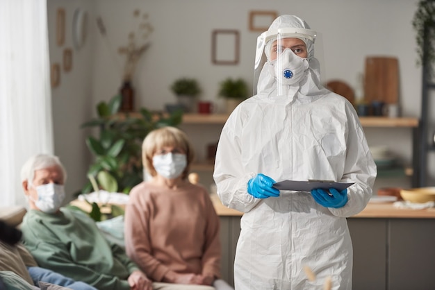 Portrait d'un médecin portant des vêtements de protection et un masque regardant la caméra lors de la visite de patients âgés à la maison