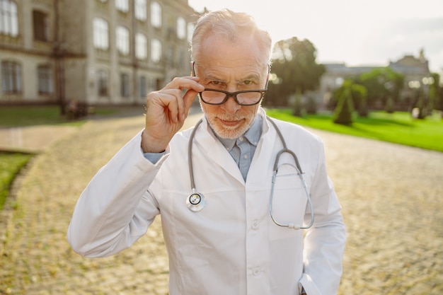 Portrait d'un médecin de sexe masculin mûr et sérieux en blouse de laboratoire ajustant ses lunettes en regardant précisément