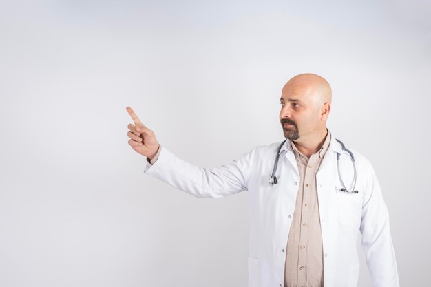 Portrait d'un médecin souriant montrant un espace de copie, médecin de sexe masculin en blouse blanche avec stéthoscope pointant.