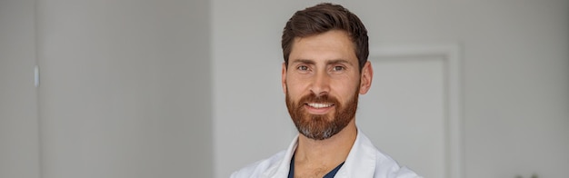 Portrait d'un médecin souriant en uniforme debout dans le hall de la clinique de médecine et regardant la caméra