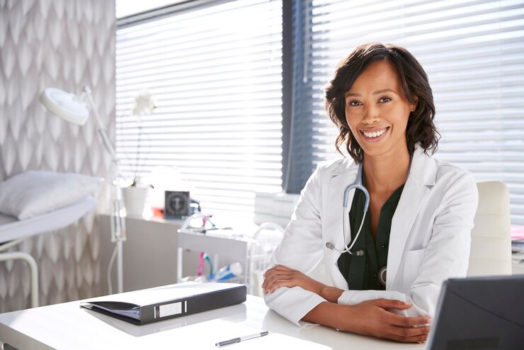 Photo portrait d'une médecin souriante portant un manteau blanc avec un stéthoscope assise derrière le bureau dans le bureau