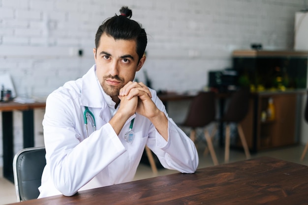 Portrait d'un médecin thérapeute sérieux portant un uniforme blanc avec stéthoscope assis au bureau dans le bureau de l'hôpital pensant en regardant vers le bas