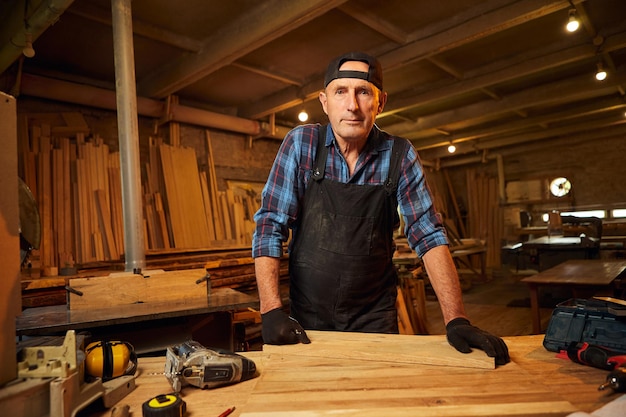 Portrait de menuisier professionnel senior en uniforme travaillant dans l'atelier de menuiserie