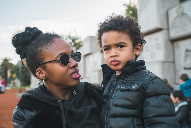 Portrait d'une mère afro-américaine avec son fils debout à l'extérieur dans le parc, s'amusant. Famille monoparentale.