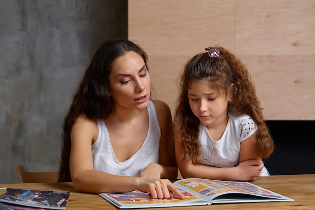 Portrait d'une mère aidant sa petite fille douce et mignonne à faire ses devoirs à l'intérieur. Famille heureuse.