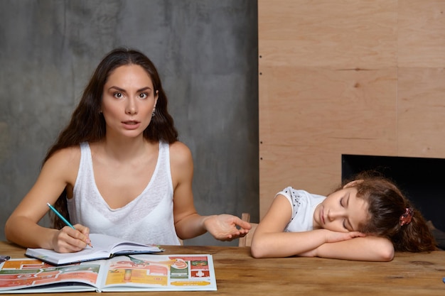 Portrait d'une mère aidant sa petite fille douce et mignonne à faire ses devoirs à l'intérieur. Famille heureuse.