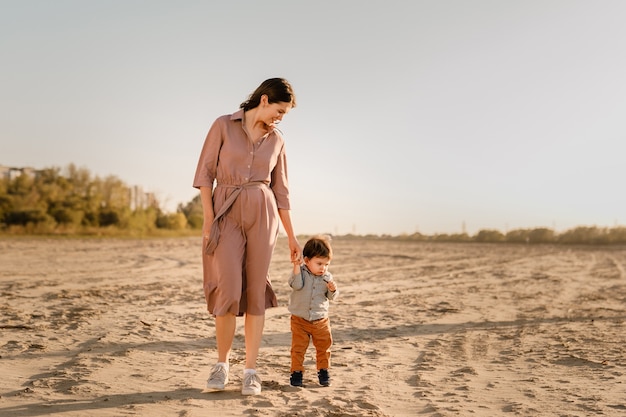 Portrait d'une mère aimante et de son fils d'un an marchant et jouant avec du sable.