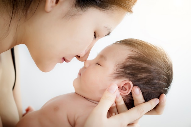 Portrait de mère asiatique heureuse utiliser nez toucher nouveau-né mignon petit bébé nez sur un lit blanc à la maison.