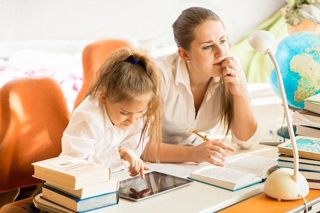 Portrait de mère assise à côté de sa fille à faire ses devoirs