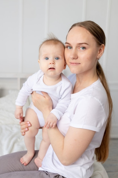 Portrait d'une mère avec un bébé dans ses bras l'embrassant doucement sur un lit blanc à la maison, l'amour de la mère