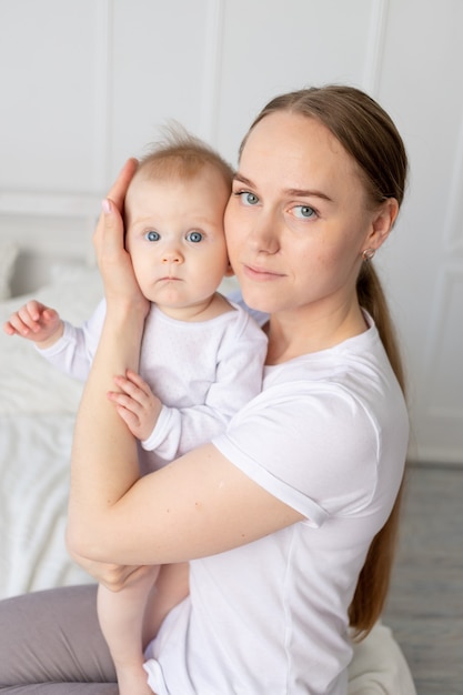 Portrait d'une mère avec un bébé dans ses bras l'embrassant doucement sur un lit blanc à la maison, l'amour de la mère.