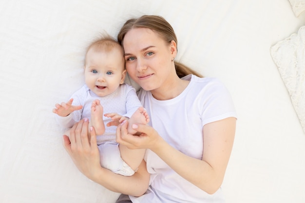 Portrait d'une mère avec un bébé dans ses bras l'embrassant doucement sur un lit blanc à la maison, l'amour de la mère