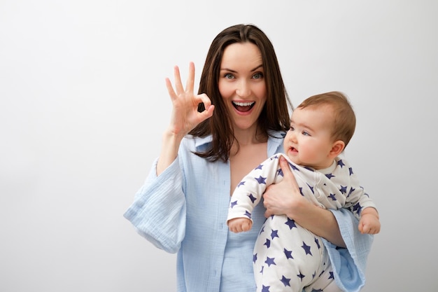 Portrait de mère et bébé femme brune souriante tient bébé et montre le geste ok avec les doigts fête des mères