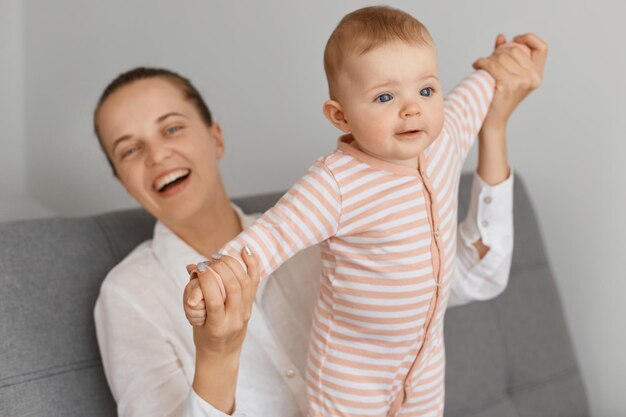 Portrait d'une mère caucasienne jouant avec son bébé, famille passant du temps ensemble, femme avec un chignon riant joyeusement alors qu'elle était assise avec sa petite fille sur un canapé.