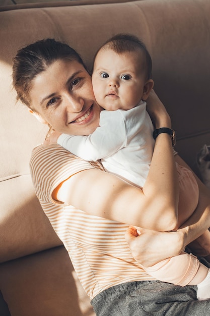 Portrait d'une mère étreignant son mignon petit enfant assis sur un canapé petite fille assise dans les bras de sa mère