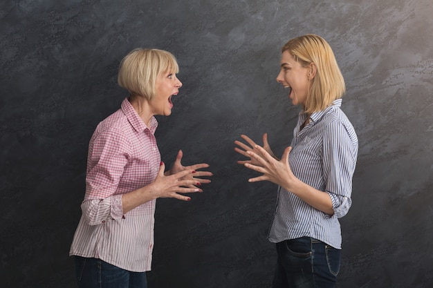 Portrait d'une mère et d'une fille adultes en colère criant l'une sur l'autre sur fond gris. Concept de génération et de relation