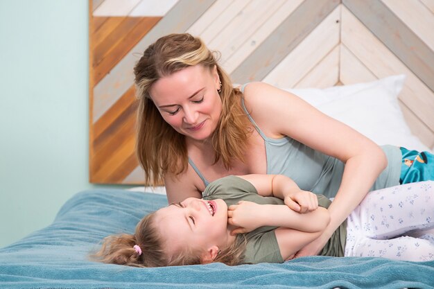 portrait de mère avec fille allongée sur le lit souriant dans la chambre, souriant l'un à l'autre,