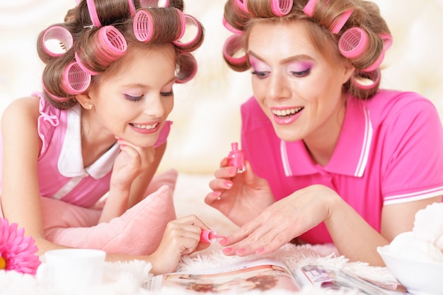 Portrait d'une mère heureuse et d'une petite fille en bigoudis avec magazine à la maison